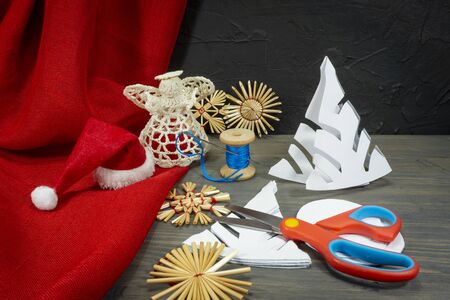Festive Xmas background with homemade Christmas decorations from straw, crocheted string and paper alongside red fabric and a pair of scissorsの写真素材