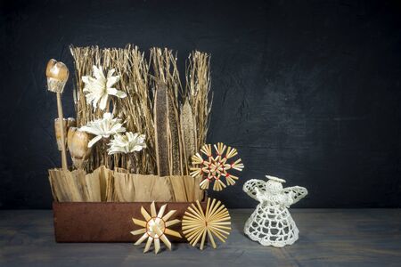 Rustic Christmas still life with handcrafted decorations of natural seeds, grasses and flowers with cute little crocheted angel over a grey background with copy spaceの写真素材
