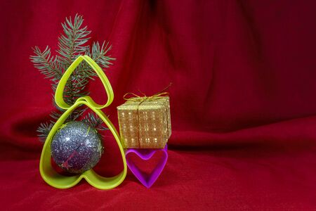 Christmas decorations with plastic hearts and small golden present box on red fabric background with copy spaceの写真素材
