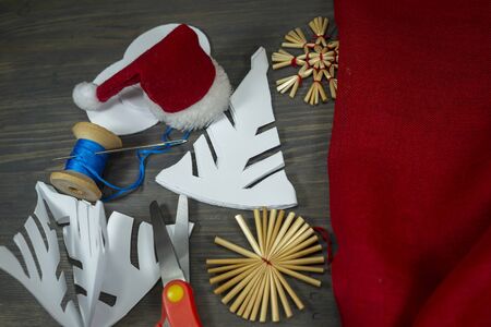 Festive Xmas background with homemade Christmas decorations from straw, crocheted string and paper alongside red fabric and a pair of scissorsの写真素材