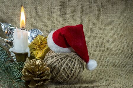 Christmas background with burning candle, decorations, gift, ball of twine and Santa hat on rustic burlap background with copy space for a holiday greetingの写真素材