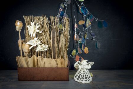 Rustic Christmas still life with handcrafted decorations of natural seeds, grasses and flowers with cute little crocheted angel over a grey background with copy spaceの写真素材