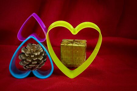 Christmas decorations with plastic hearts and small golden present box on red fabric background with copy spaceの写真素材