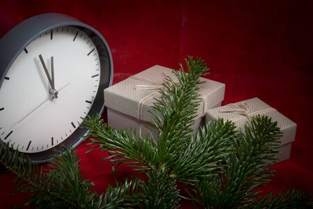 Christmas still life with a clock , gifts and pine branches over a festive red background with vignette and copy space for a seasonal greetingの写真素材