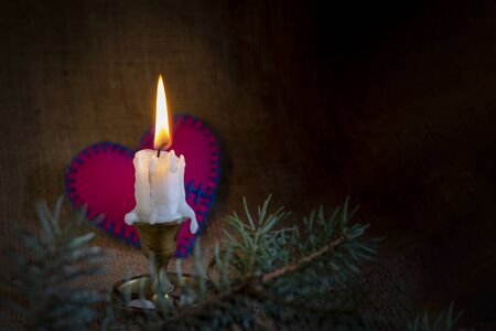 Burning candle on a vintage candlestick and a small red stitched fixed broken heart in the dark against sack cloth background with copy space. Magical love spell conceptの写真素材
