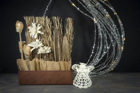 Rustic Christmas still life with handcrafted decorations of natural seeds, grasses and flowers with cute little crocheted angel over a grey background with copy spaceの写真素材