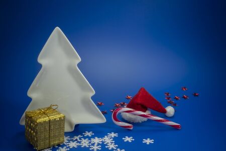Festive blue Christmas still life with gifts, decorative Christmas tree shape plate, candy cane and a colorful red Santa hat with copy space for a holiday greetingの写真素材