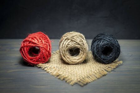 Three balls of natural hemp twine with coarse fibers in a natural brown, red and black with a square of hessian over a rustic wood grey backgroundの写真素材