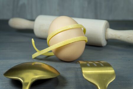Homemade Italian pasta with whole fresh raw egg ingredient in a low angle still life viewed over gold cutlery with rolling pin in the backgroundの写真素材