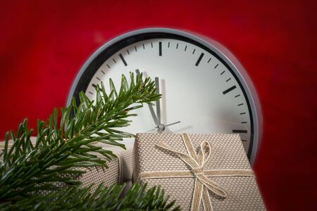 Christmas still life with a clock , gifts and pine branches over a festive red background with vignette and copy space for a seasonal greetingの写真素材