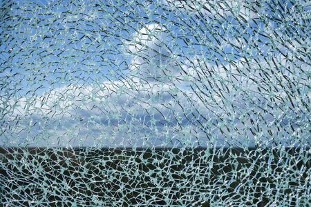 Cracked laminated glass surface against blue sky with white clouds blurred in background