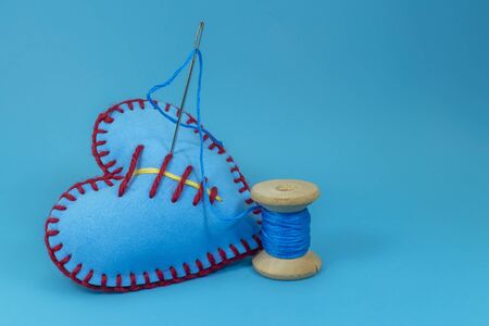 Hand stitched fabric heart and spool of thread with needle on blue background, handmade sewing, needlework and tailoring conceptの写真素材