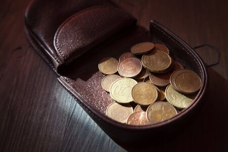 Euros coins change in open dark brown hard leather coin case tray purse or wallet, viewed in close-up on wooden tableの写真素材