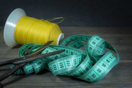 Old metal scissors with tape measure and spools of thread on rustic wooden background, needlework...