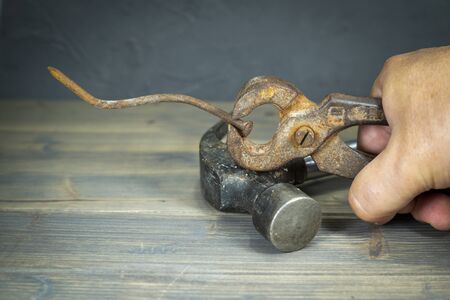 Male hand holding old rusty grips and long bent corroded nail over a rustic wooden table in a close up viewの写真素材