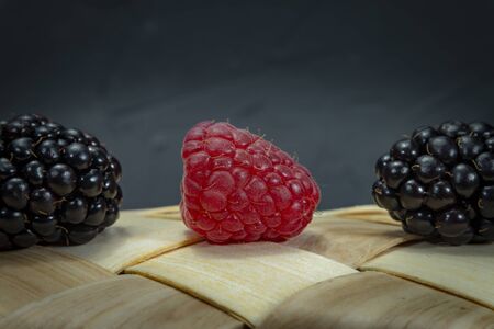 Close up of one fresh ripe raspberry and two blackberries on a tipped wicker basket