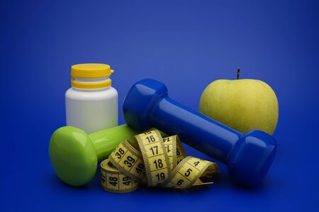 Still life with small dumbbells, measuring tape and fruits, as a concept of healthy nutrition and sports diet in close-up on blue backgroundの写真素材