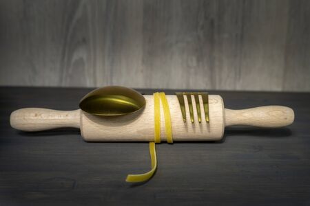 Homemade Italian pasta with whole fresh raw egg ingredient gold cutlery with rolling pin in a low angle still lifeの写真素材