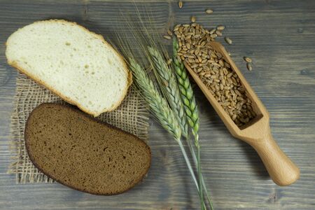 Fresh ears and grains of wheat with sliced white and brown or wholegrain bread on hessian on a rustic wooden table viewed from overhead as a flat layの写真素材