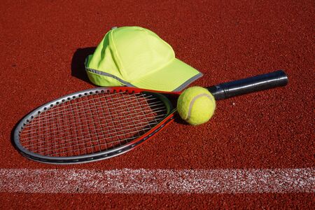 Tennis racket on all weather outdoor court, peaked cap and balls in a sports and healthy lifestyle conceptの写真素材