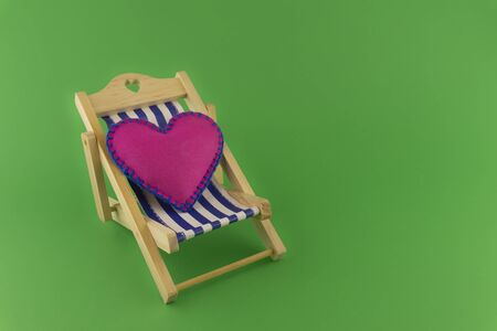 Romantic pink heart on a striped deck chair over a green background symbolic of love, an engagement, wedding or Valentines Dayの写真素材