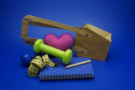 Going shopping for sports diet concept still life with dumbbells, measuring tape and notebook on blue backgroundの写真素材