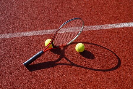 Tennis ball, line and racket on an outdoor court with the racket standing on end casting a shadow across the all weather surfaceの写真素材