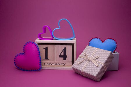 Pink and blue handcrafted fabric hearts symbolising Love in a Valentines Day background with wooden date decorated with heart-shaped cookie cutters and gift over magenta pinkの写真素材
