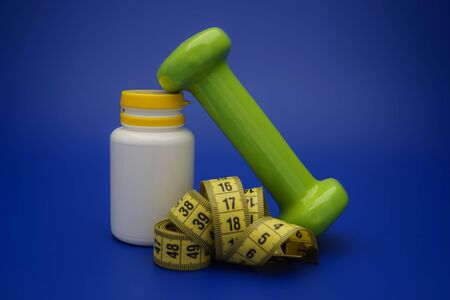 Still life with small dumbbells, measuring tape and white medicine bottle, as a concept of healthy nutrition and sports diet in close-up on blue backgroundの写真素材