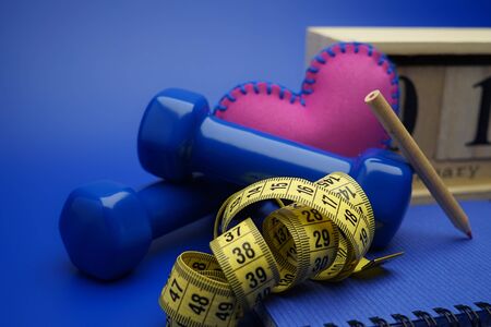 Starting healthy lifestyle on the first day of the year concept. Still life with dumbbells, measuring tape, calendar and new notebook on blue backgroundの写真素材