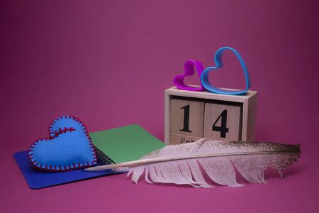Valentines Day still life with hand sewn textile pink and blue hearts flanking a wooden date decorated with matching heart-shaped cookie cutters, quill pen and notebookの写真素材