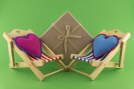 Romantic still life with pink and blue hearts on small toy deck chairs and wrapped gift over green for Valentines Day or a weddingの写真素材