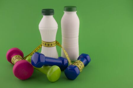 Weight loss and fitness concept with tape measure wound round a white plastic bottle with a slim line shape, pink and blue dumbbells on green chroma key backgroundの写真素材