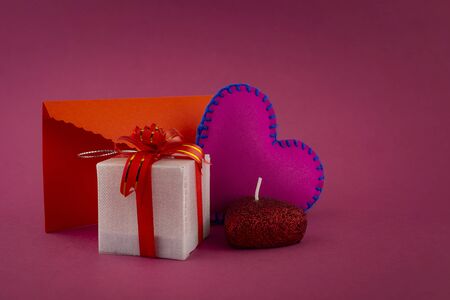 Romantic still life with purple glowing heart, decorative gifts and red envelope on pink background with copy spaceの写真素材