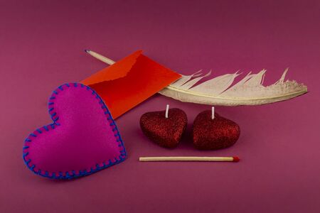 Heart-shaped candles and an envelope for writing Valentines Day letter concept, with a feather and a match for lighting candles. Love and romantic message still life on red backgroundの写真素材