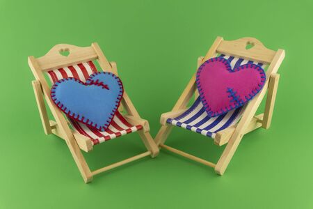 Romantic still life with pink and blue hearts on small toy deck chairs over green for Valentines Day or a wedding tripの写真素材