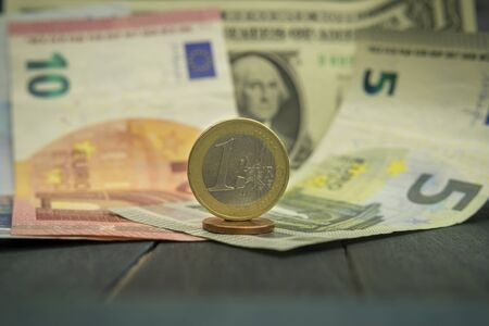Close-up of Euro and USD cash money with various coins of Euros and cents over banknotes on black wooden table. Strong and stable currency concept with dollar bill and variety of Euro billsの写真素材