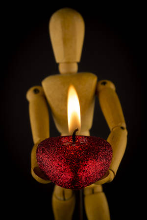 Wooden puppet or figure holding a burning red candle over a dark background in a conceptual imageの写真素材