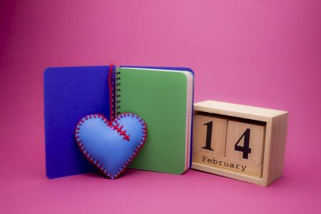 Valentines Day still life with hand sewn textile blue heart, notebook and wooden date over a pink backgroundの写真素材