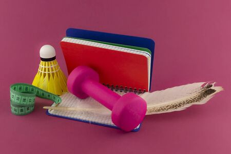 Sport weight loss and fitness concept with a shuttlecock, dumbbell weight and tape measure alongside an open notebook wit quill pen on a bright pink backgroundの写真素材