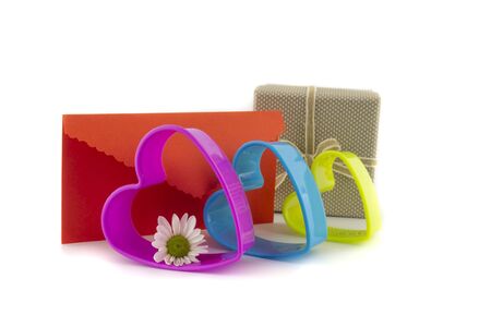 Valentines gift with a colorful row of plastic cookie cutter hearts and decorative orange love letter over a white background with fresh white spring daisyの写真素材