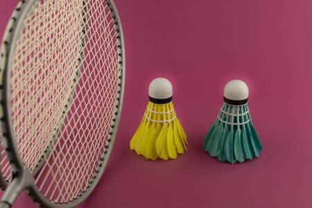 Badminton rackets and colorful feathered shuttlecocks in blue and yellow on a pink backgroundの写真素材