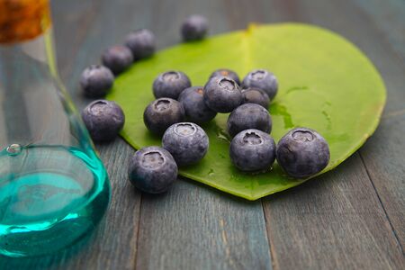 Ripe blueberries spilling onto a green leaf on a dark blue wooden table with blue solution in a flask alongside in a health and nutritional concept with copy spaceの写真素材