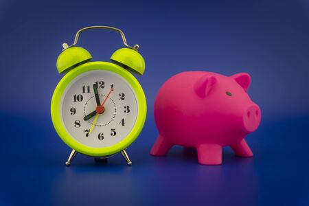 Pink piggy bank and analog alarm clock on blue background, time to start saving conceptの写真素材