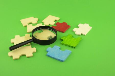 Selection of jigsaw puzzle pieces with magnifying glass on a green background with copy space...