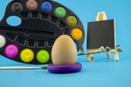 Easter egg decoration concept with paint brushes and set of watercolor paints in pallet. Studio still life on blue backgroundの写真素材