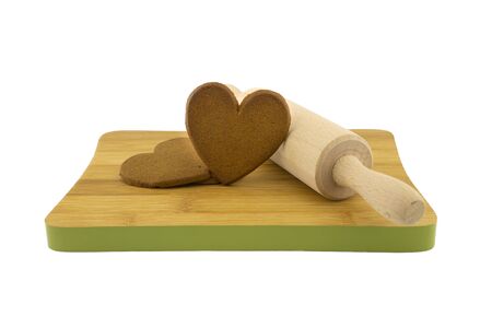Heart-shaped cookies gift preparation concept with brown biscuits and rolling pin on wooden cutting board isolated on white backgroundの写真素材