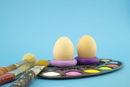 Easter eggs coloring concept with three unpainted eggs and set of different paint brushes, on blue backgroundの写真素材