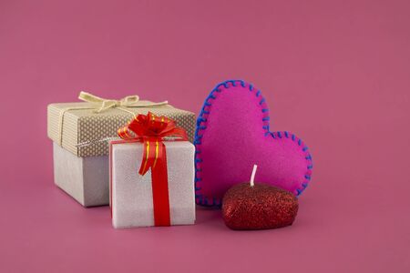 Romantic still life with hand sewn textile pink heart, candle, decorative gifts and red envelope on pink background with copy spaceの写真素材