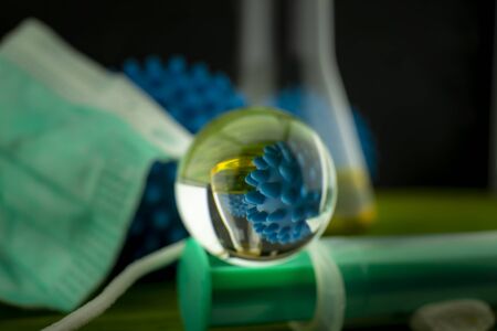 Glass sphere reflecting a surgical mask and blue virus molecule within the orb conceptual of the coronavirus or Covid-19 pandemic with copy space alongsideの写真素材